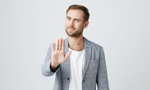 Angry bearded male model gestures indoors, shows stop sign with palm, refuses to do something, isolated against gray studio background. Serious bearded irritated man shows stop gesture indoors Angry bearded male model gestures indoors, shows stop sign with palm, refuses to do something, isolated against gray studio background. Serious bearded irritated man shows stop gesture indoors